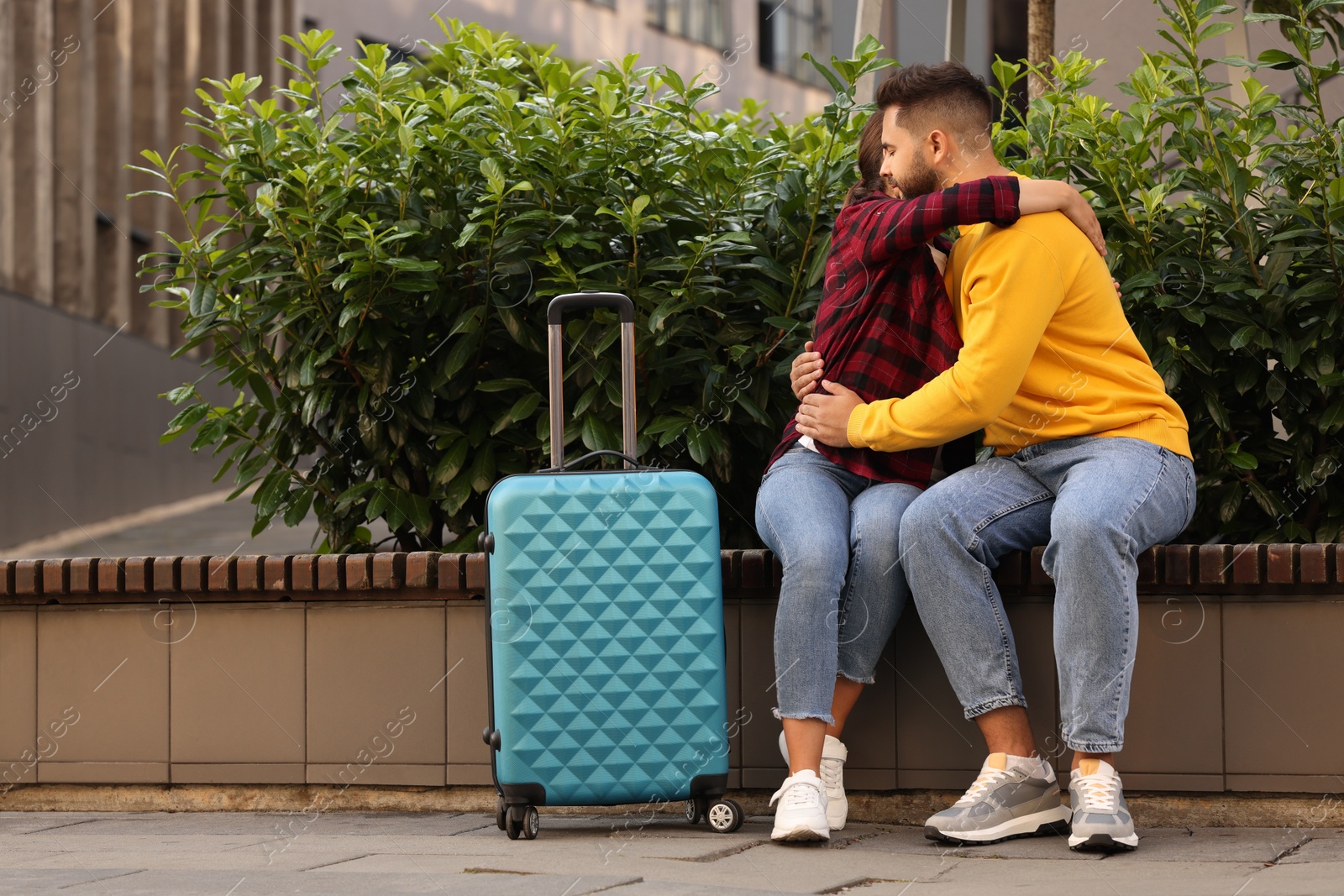 Photo of Long-distance relationship. Beautiful couple hugging on bench and suitcase outdoors