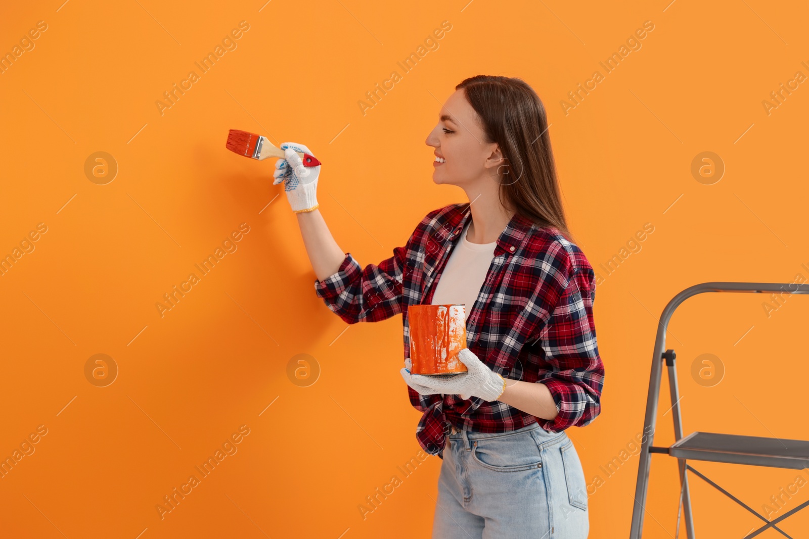 Photo of Happy designer painting orange wall with brush