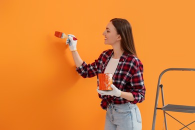 Photo of Happy designer painting orange wall with brush