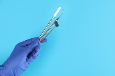 Photo of Dentist holding set of tools on light blue background, closeup. Space for text