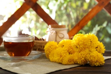 Photo of Beautiful yellow chrysanthemum flowers and cup of aromatic tea on wooden table