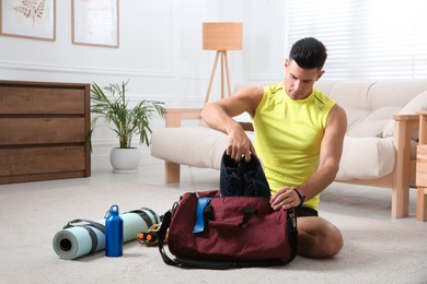 Man packing sports stuff for training into bag at home