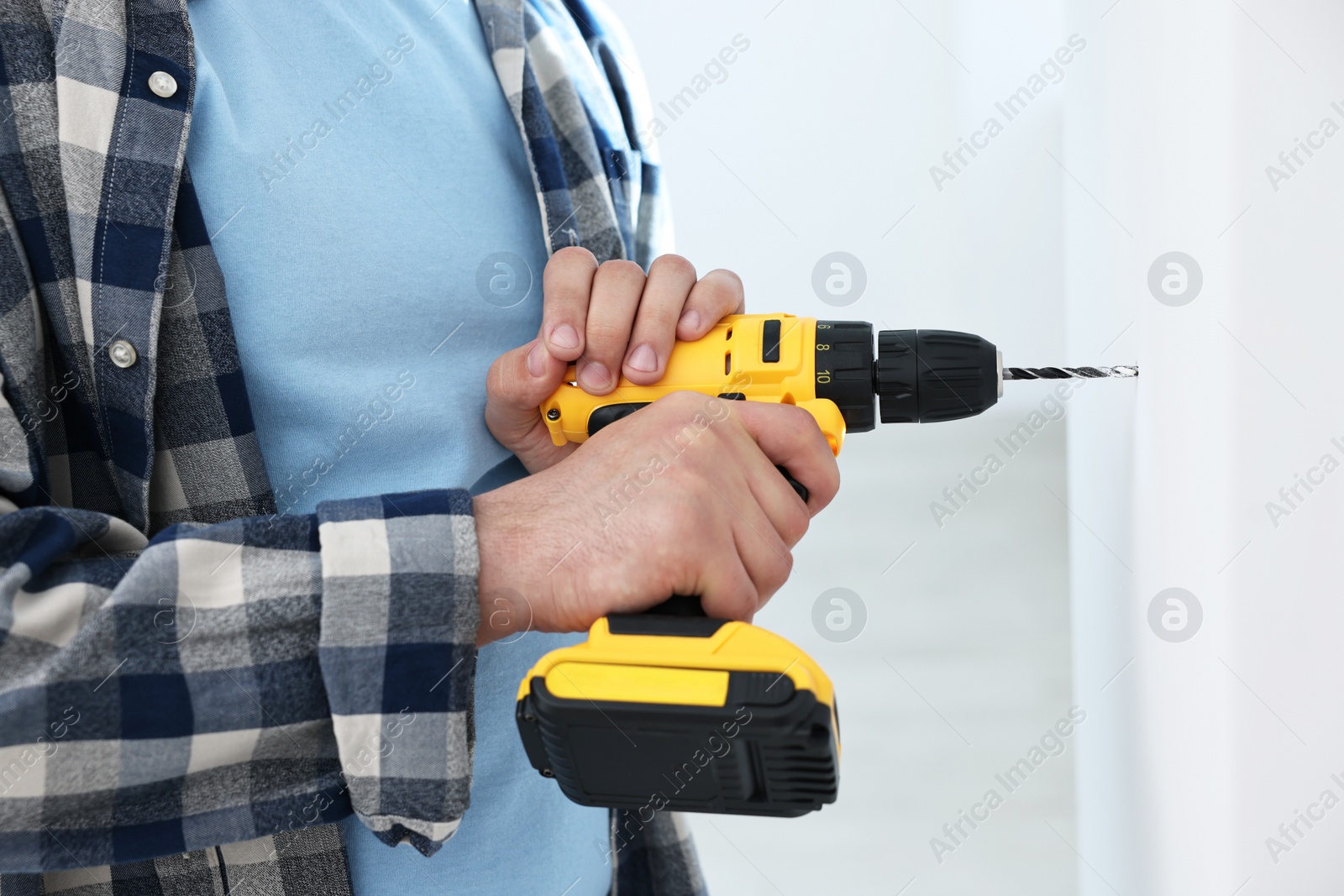 Photo of Young handyman working with electric drill at home, closeup