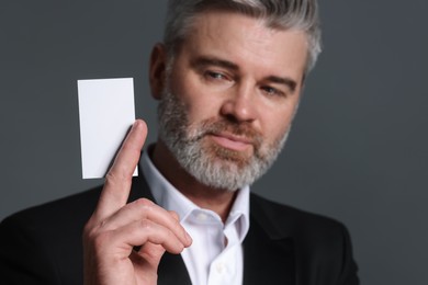 Handsome man holding blank business card on grey background, selective focus