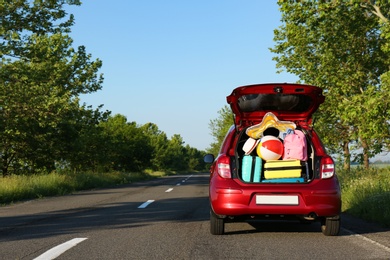 Family car with open trunk full of luggage on highway. Space for text