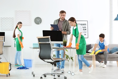 Team of professional janitors in uniform cleaning office