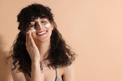 Photo of Beautiful young woman applying sun protection cream onto face on beige background, space for text