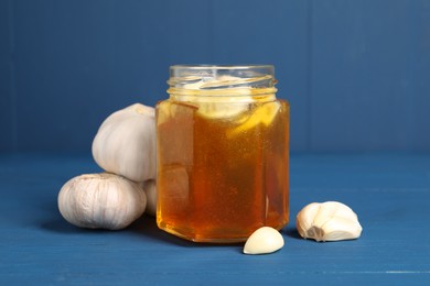 Photo of Honey with garlic in glass jar on blue wooden table