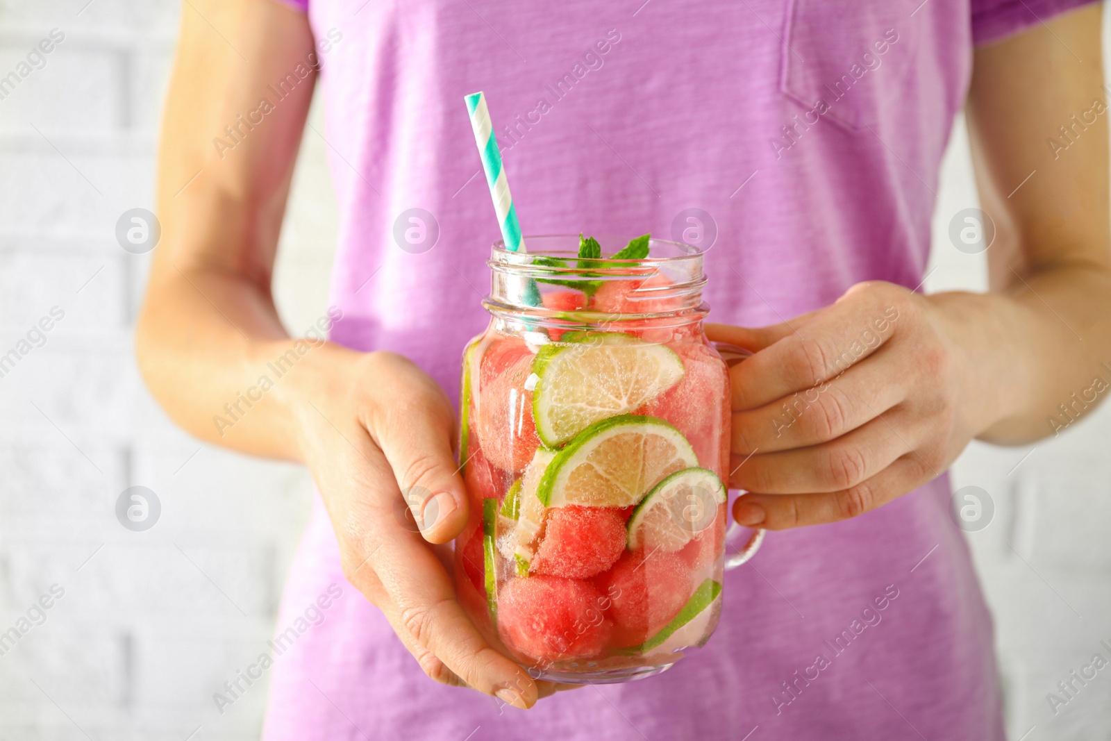 Photo of Young woman with tasty refreshing watermelon drink near light wall, closeup