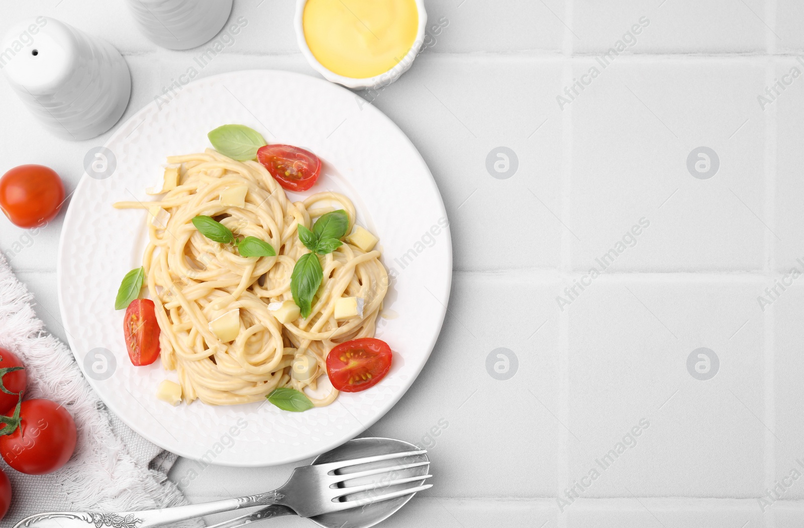 Photo of Delicious pasta with brie cheese, tomatoes and basil leaves on white tiled table, flat lay. Space for text