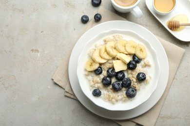 Tasty oatmeal with banana, blueberries, butter and milk served in bowl on light grey table, flat lay. Space for text