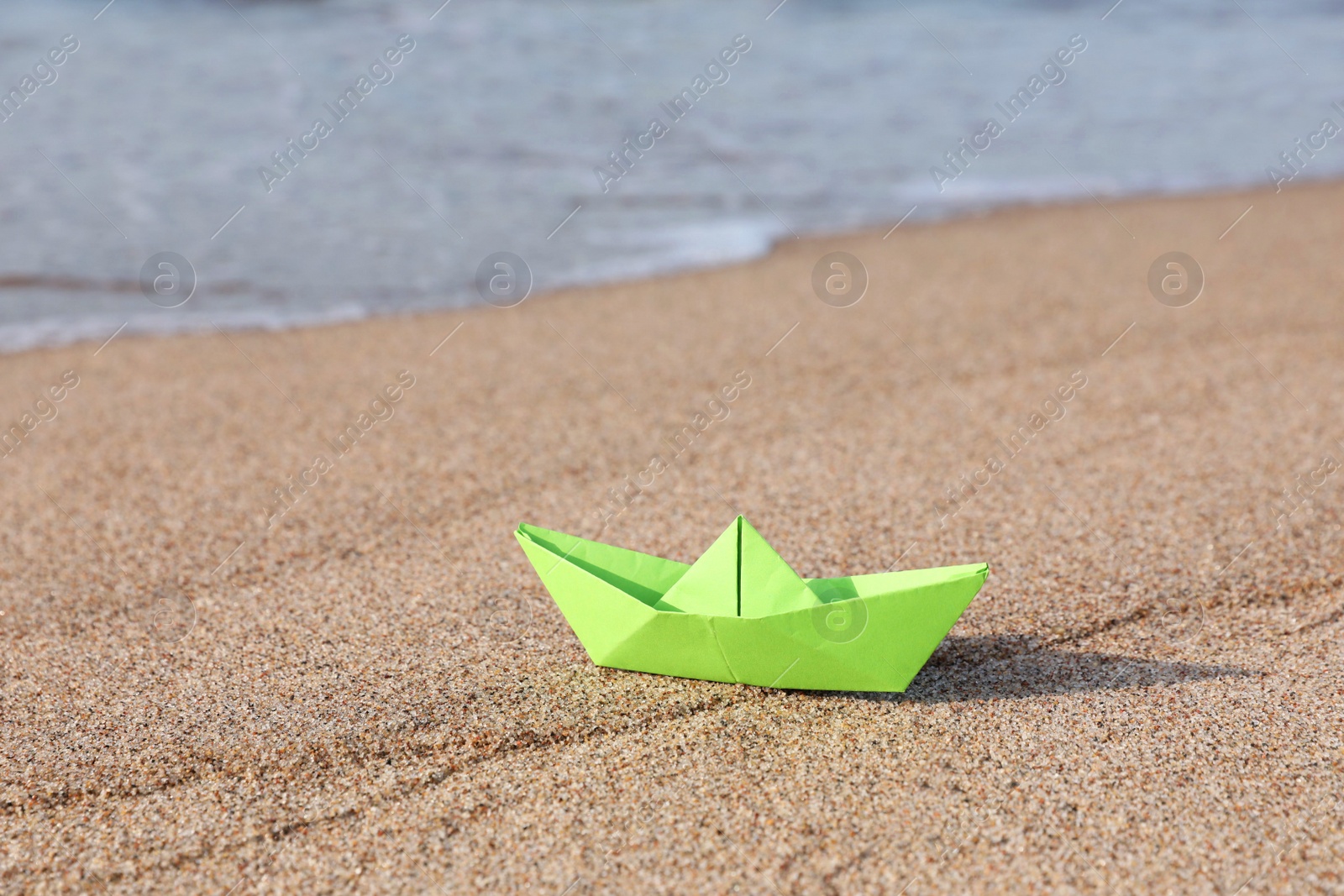 Photo of Light green paper boat near sea on sandy beach