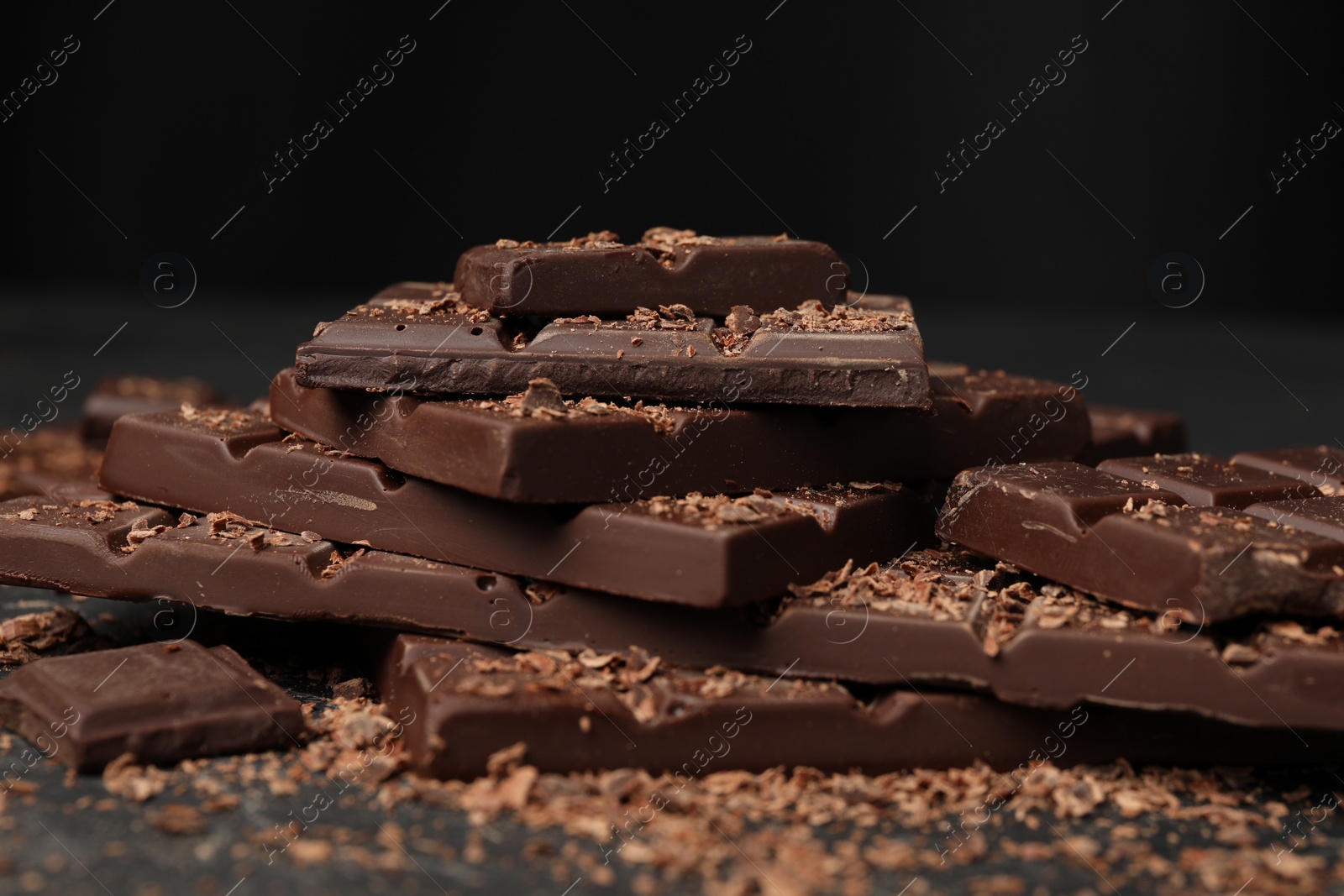 Photo of Pieces and shavings of tasty chocolate on dark table, closeup