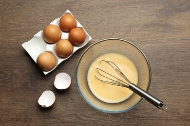 Photo of Beaten eggs and whisk on wooden table, flat lay
