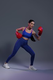 Photo of Beautiful woman wearing boxing gloves training in color lights on grey background