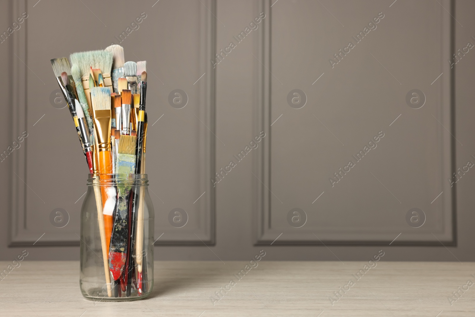 Photo of Different paintbrushes in glass jar on white wooden table. Space for text