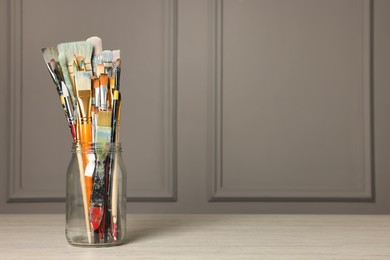 Different paintbrushes in glass jar on white wooden table. Space for text