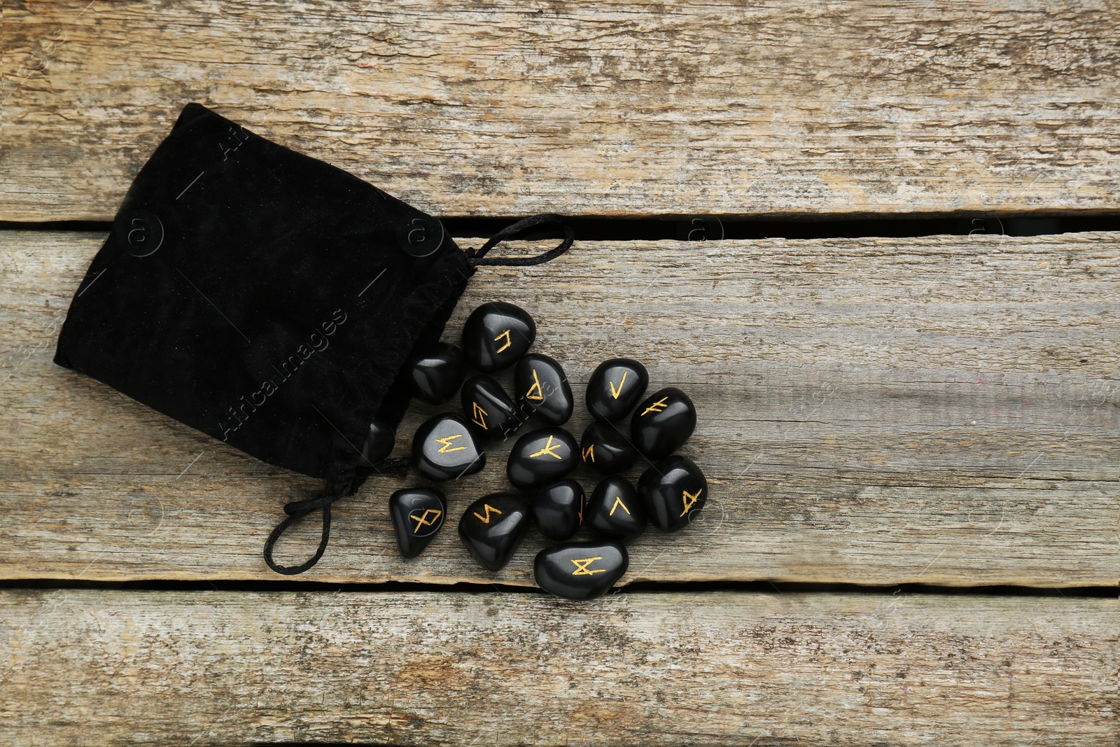 Photo of Bag with black rune stones on wooden table, flat lay