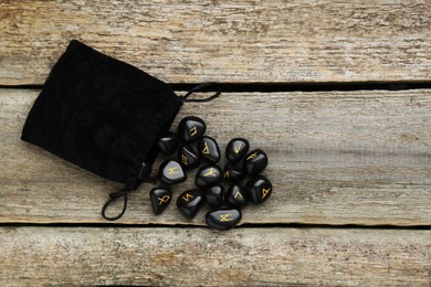 Bag with black rune stones on wooden table, flat lay