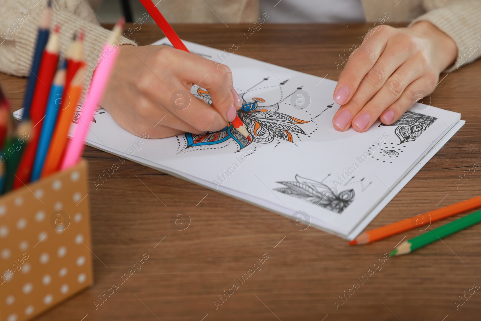 Photo of Young woman coloring antistress page at table, closeup