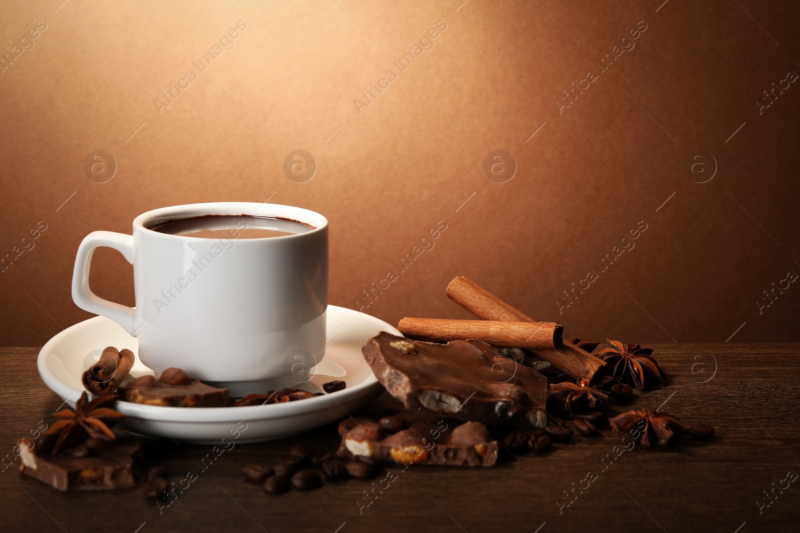 Photo of Cup of delicious hot chocolate, spices and coffee beans on wooden table. Space for text