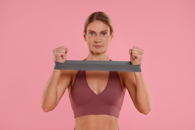 Photo of Woman exercising with elastic resistance band on pink background