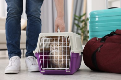 Photo of Travel with pet. Man near carrier with cute cat at home, closeup