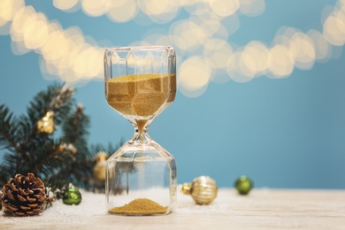 Photo of Hourglass, fir tree twigs and decor on white table against blurred lights, space for text. Christmas countdown