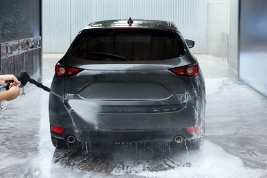 Photo of Man washing auto with high pressure water jet at car wash, closeup