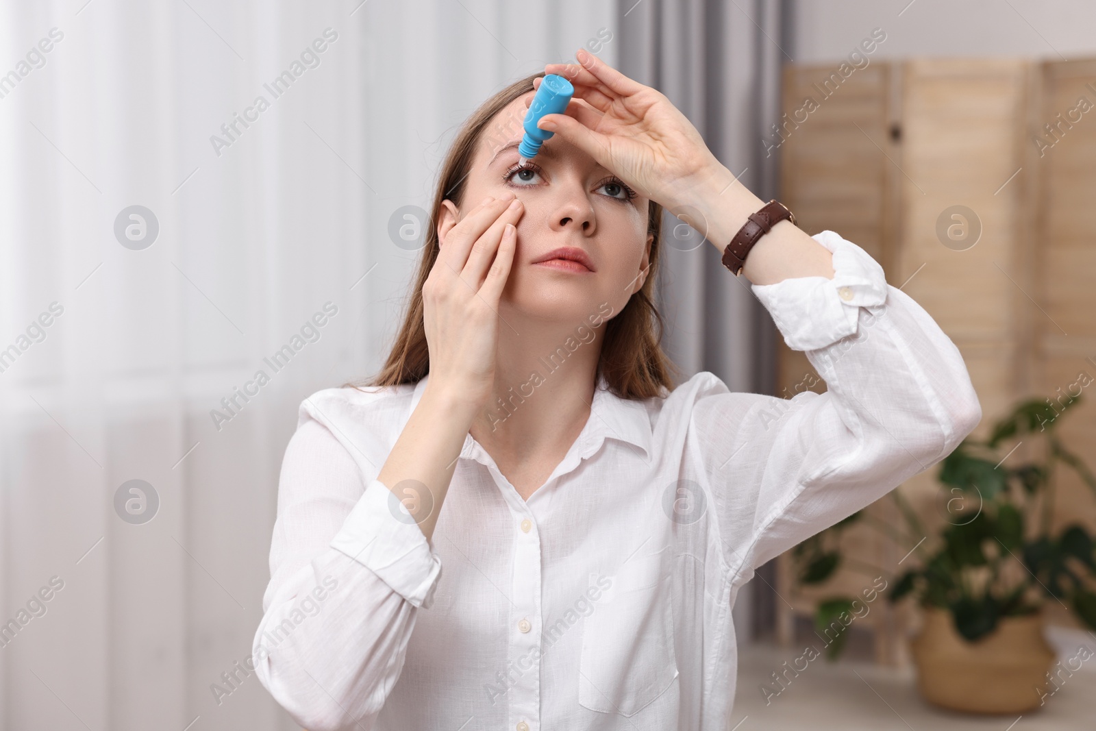 Photo of Young woman applying medical eye drops indoors