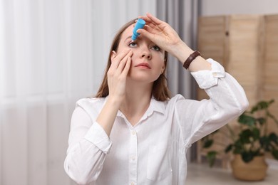 Young woman applying medical eye drops indoors