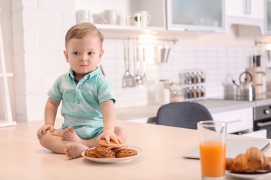 Photo of Cute little boy with cookies sitting on table in kitchen