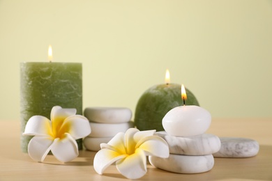 Photo of Composition of spa stones, flowers and burning candles on wooden table against light green background