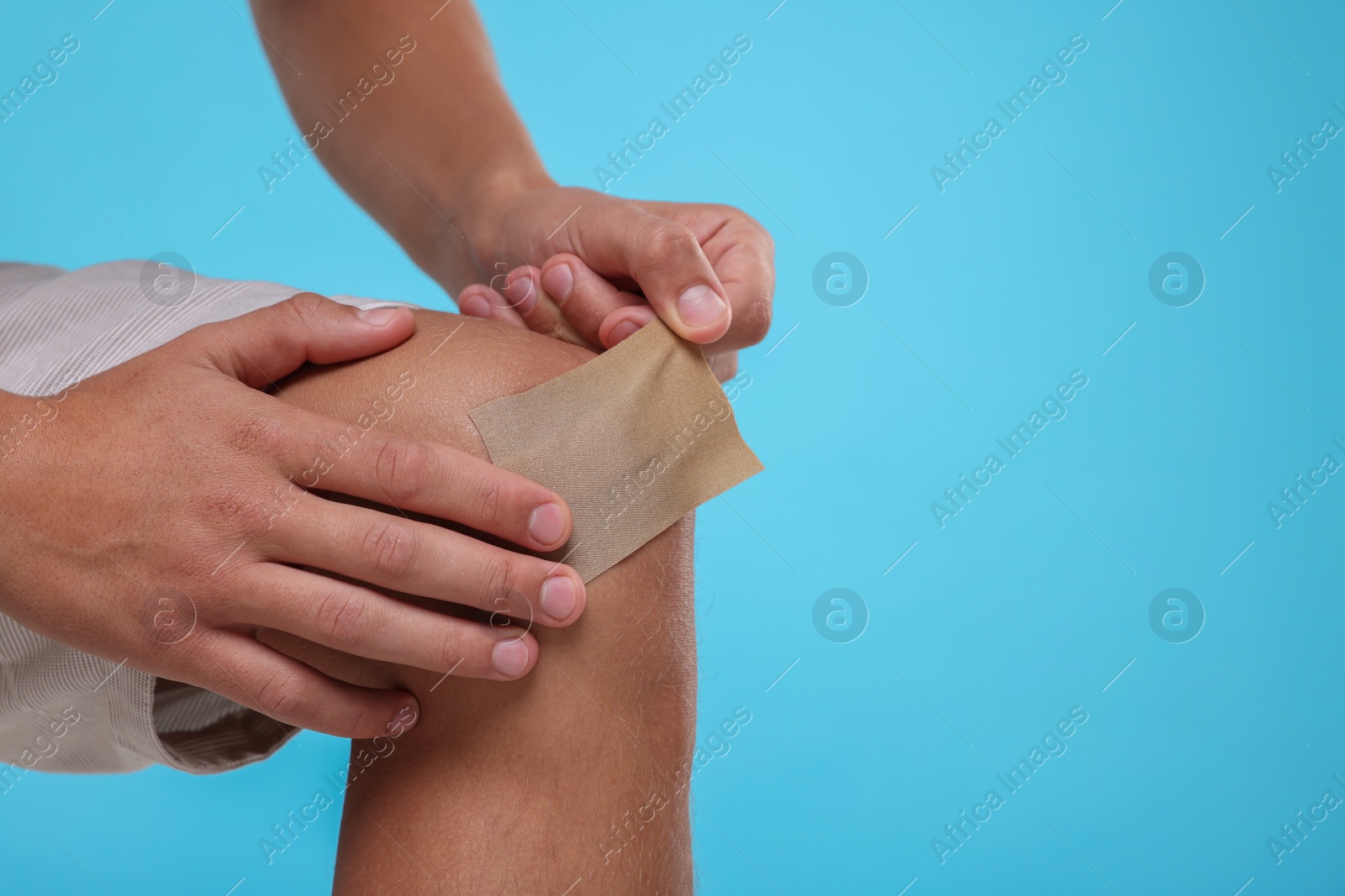 Photo of Man putting sticking plaster onto knee on light blue background, closeup. Space for text