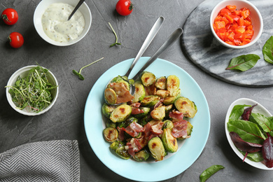 Photo of Delicious roasted Brussels sprouts with bacon served on black table, flat lay