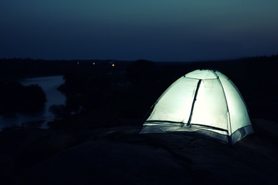 Photo of Small camping tent glowing in twilight outdoors. Space for text