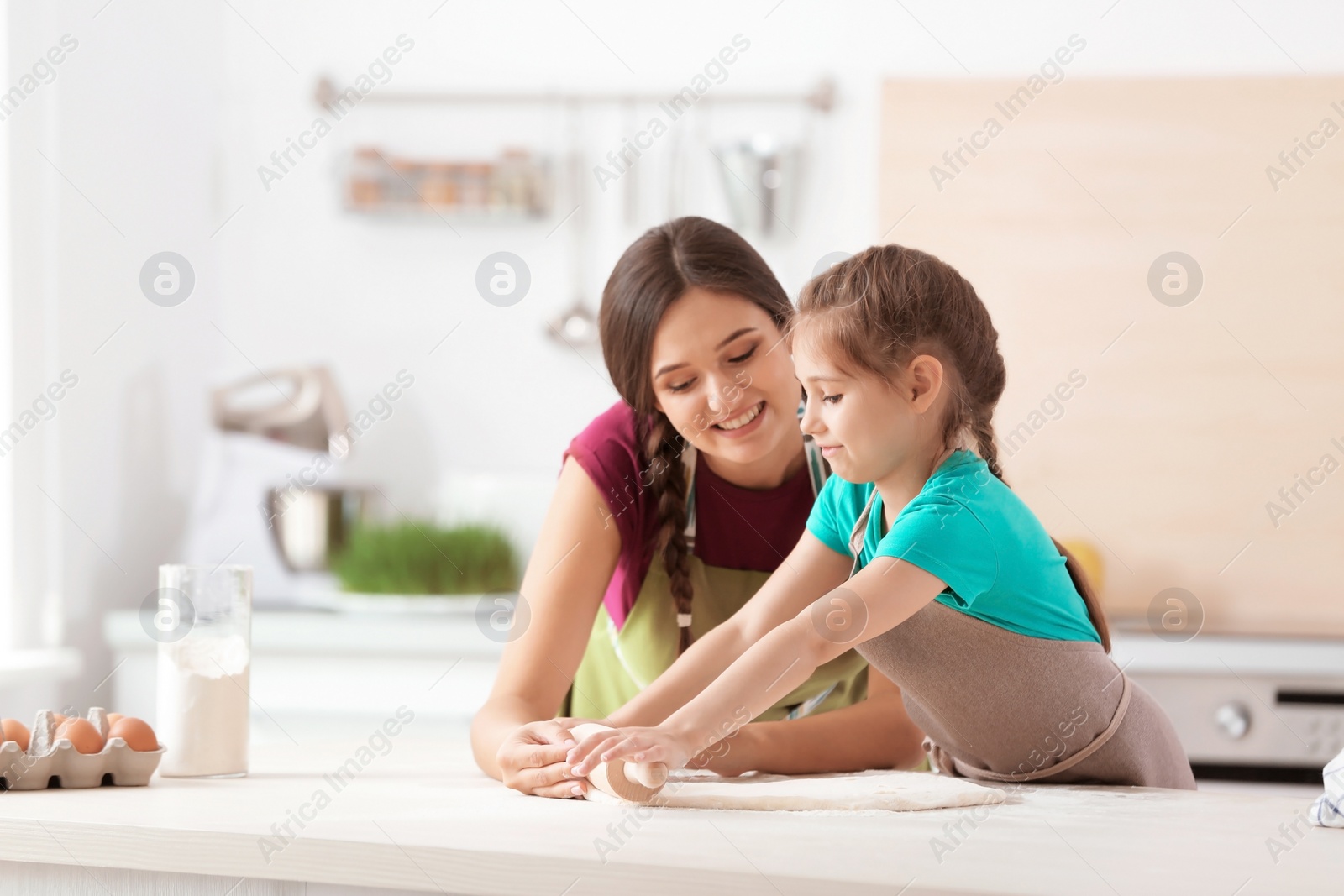 Photo of Mother and her daughter preparing dough at table in kitchen