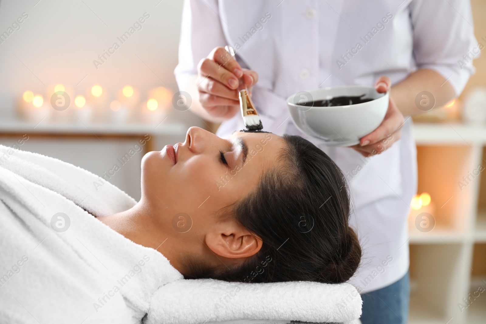 Photo of Cosmetologist applying mask onto woman's face in spa salon