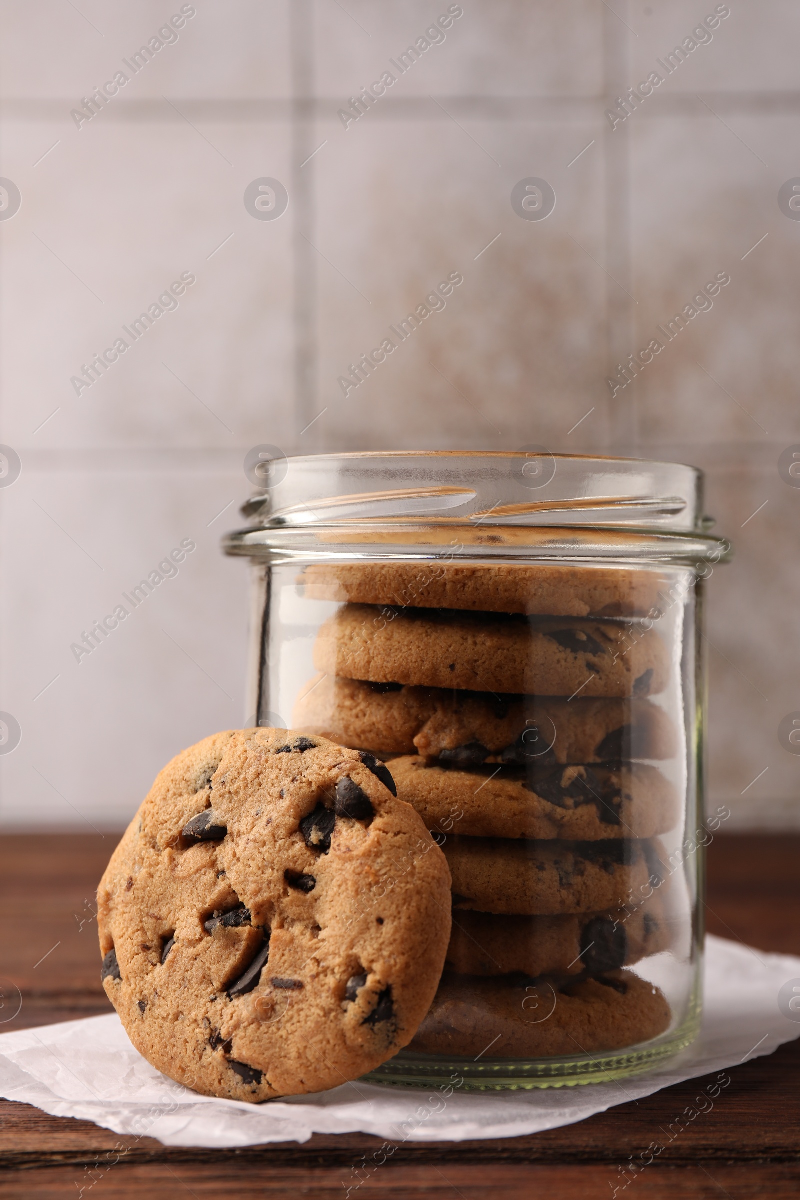 Photo of Glass jar with delicious chocolate chip cookies on wooden table