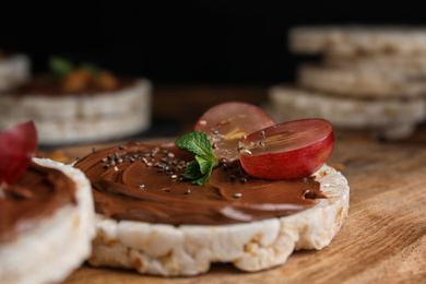 Photo of Puffed rice cake with chocolate spread and grape on wooden board, closeup