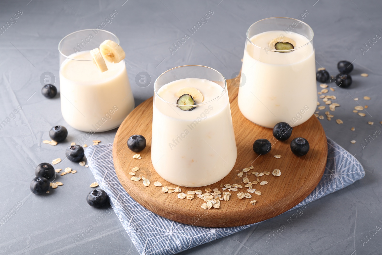 Photo of Tasty yogurt in glasses, oats and blueberries on grey table