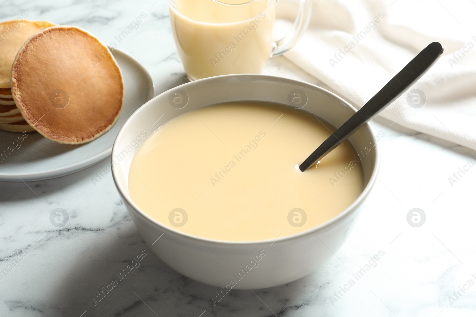 Photo of Bowl with condensed milk served on marble table, closeup. Dairy products