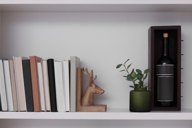 Shelf with houseplant, books and wine bottle near beige wall. Interior design