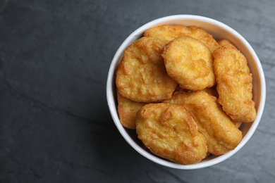 Bucket with tasty chicken nuggets on black table, top view. Space for text