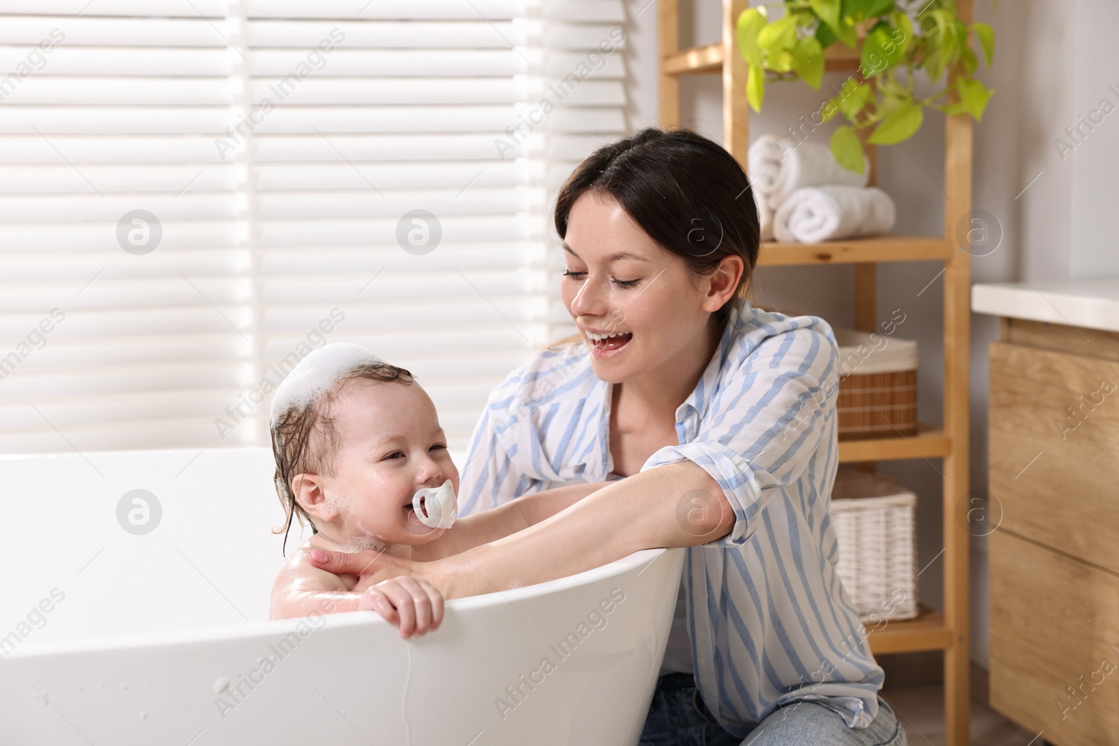 Photo of Mother bathing her cute little baby in tub at home