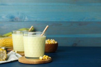 Photo of Tasty fresh corn milk in glasses and cobs on blue wooden table. Space for text