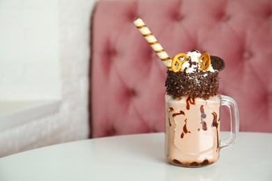 Tasty milk shake with sweets in mason jar on table at cafe. Space for text