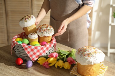 Photo of Woman putting traditional Easter cakes in basket indoors, closeup