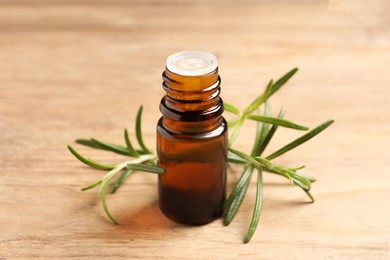 Photo of Bottle with essential oil and fresh rosemary on wooden table