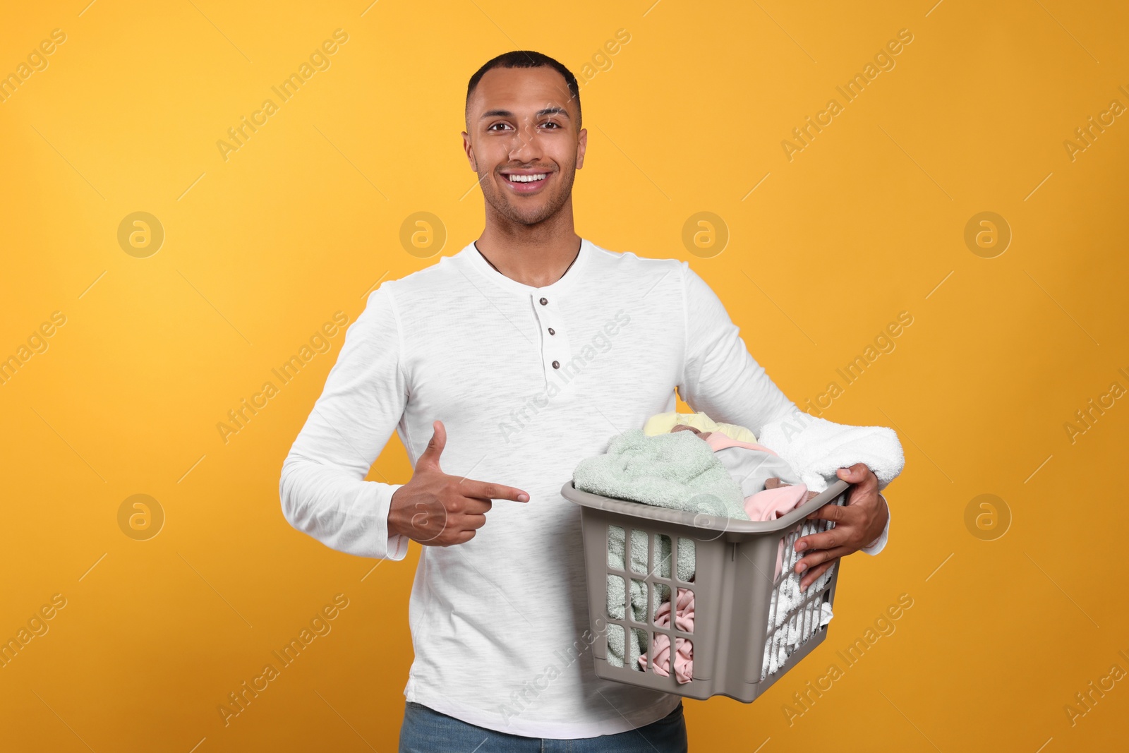 Photo of Happy man with basket full of laundry on orange background